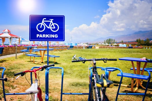 A bicycle is parked in a land lot with lush green grass under a cloudy sky, surrounded by nature and asphalt landscape