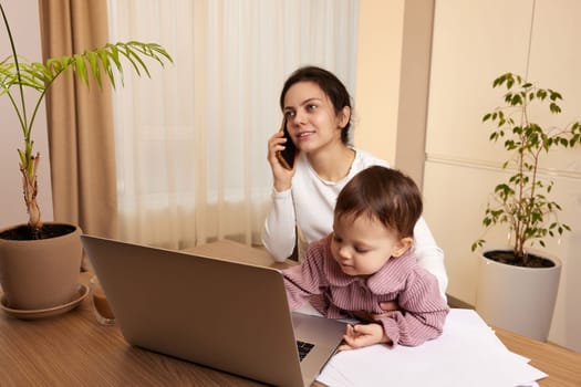 Cheerful pretty businesswoman working at home with her little child girl