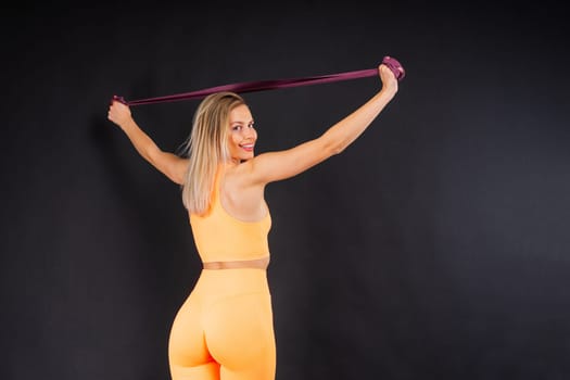 Sports woman in fashion sportswear exercising with elastic band in a studio