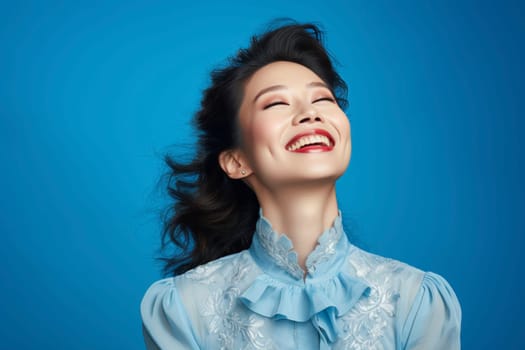 Portrait of a joyful woman laughing with closed eyes. Studio photography with blue background. Happiness and beauty concept. Design for advertisement, poster