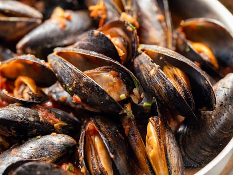 Delicious black mussels in red tomato sauce close up. Mediterranean black mussels in metal pan.