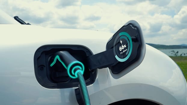 Electric car plug in with charging station, recharge battery by EV charger cable display smart digital battery status hologram with nature background. Futuristic green energy infrastructure.Peruse