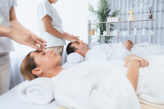 Caucasian couple enjoying relaxing anti-stress head massage and pampering facial beauty skin recreation leisure in dayspa modern light ambient at luxury resort or hotel spa salon. Quiescent