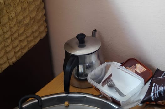 A pot of water sits on a hardwood table next to a kettle in a room with wood flooring, inside a building with a high ceiling