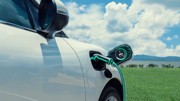 Electric car plug in with charging station, recharge battery by EV charger cable display smart digital battery status hologram with nature background. Futuristic green energy infrastructure.Peruse