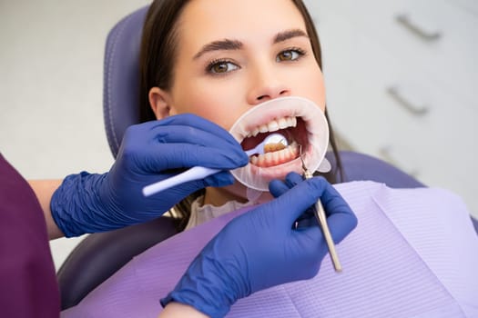 Portrait of young woman in dental clinic. Dentist in rubber gloves doing check up.