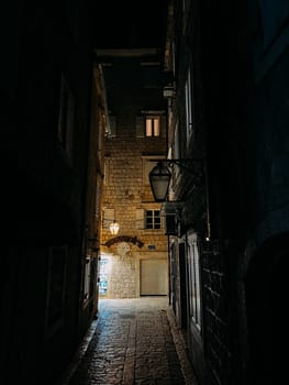 Narrow street of an ancient town with stone buildings illuminated by lanterns at night. High quality photo
