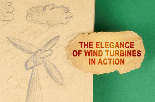 Alternative energy concept. On a green surface there is a drawing with a wind generator and a cardboard with the inscription - The elegance of wind turbines in action