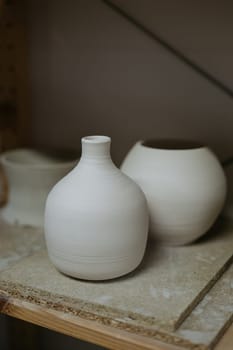 A row of unfinished white ceramic vases on a studio shelf.