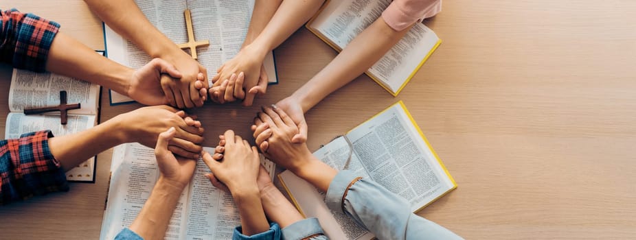 Cropped image of group of people praying together while holding hand on holy bible book at wooden church. Concept of hope, religion, faith, christianity and god blessing. Top view. Burgeoning.