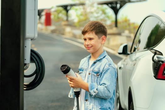 Little boy recharging eco-friendly electric car from EV charging station. EV car road trip travel concept for alternative transportation powered by clean renewable and sustainable energy. Perpetual