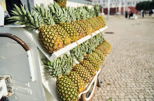 A cart filled with pineapples, a type of terrestrial plant and fruit, on a cobblestone street. The pineapples are a natural whole food, also known as Ananas