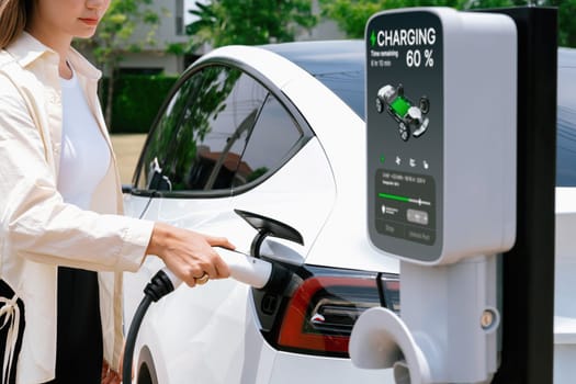 Young woman put EV charger to recharge electric car's battery from charging station. Alternative energy and rechargeable EV car for sustainable environmental friendly travel concept. Expedient