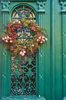 A wooden home door adorned with a wreath made of green flowers, adding a charming fixture to the facade of the building and creating symmetry on the wall