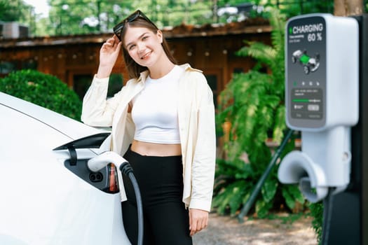 Young woman and sustainable urban commute with EV electric car recharging at outdoor cafe in springtime garden, green city sustainability and environmental friendly EV car. Expedient