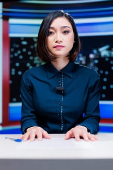 Presenter on midnight news show addressing media outlets information about international events during live segment. Asian woman talking about international newscast with details.
