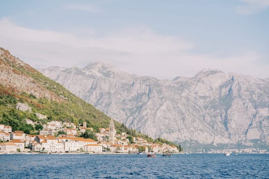 Ancient houses of Perast on the shore of the Bay of Kotor with an ancient bell tower against the backdrop of the mountains. Montenegro. High quality photo