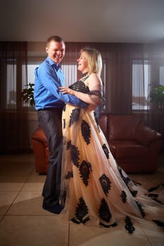 A plump woman in royal dress and a skinny man together in honeymoon hotel room. An adult newlywed couple embraces in an intimate setting. Queen Girl and guy in love