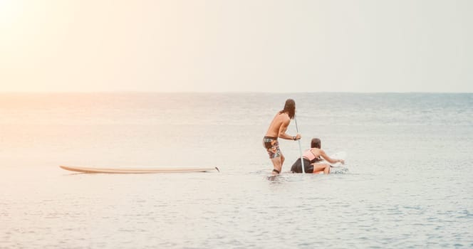 Sea woman and man on sup. Silhouette of happy young woman and man, surfing on SUP board, confident paddling through water surface. Idyllic sunset. Active lifestyle at sea or river