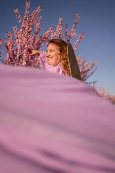 Woman blooming peach orchard. Against the backdrop of a picturesque peach orchard, a woman in a long pink dress and hat enjoys a peaceful walk in the park, surrounded by the beauty of nature