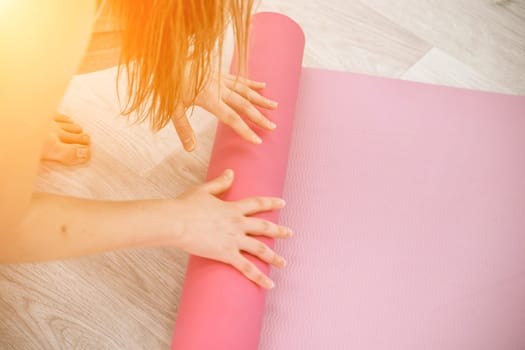 A young woman rolls a pink fitness or yoga mat before or after exercising, exercising at home in the living room or in a yoga studio. Healthy habits, keep fit, weight loss concept. Closeup photo.