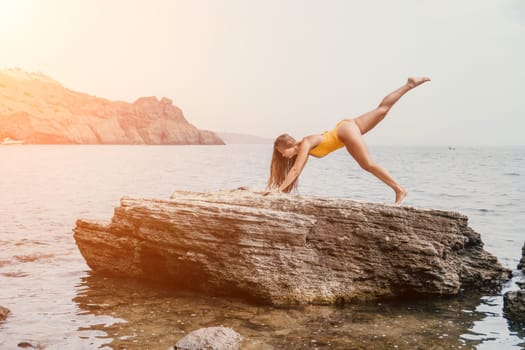 Woman meditating in yoga pose silhouette at the ocean, beach and rock mountains. Motivation and inspirational fit and exercising. Healthy lifestyle outdoors in nature, fitness concept.