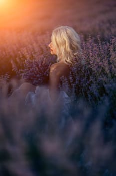 Blonde woman poses in lavender field at sunset. Happy woman in white dress holds lavender bouquet. Aromatherapy concept, lavender oil, photo session in lavender.