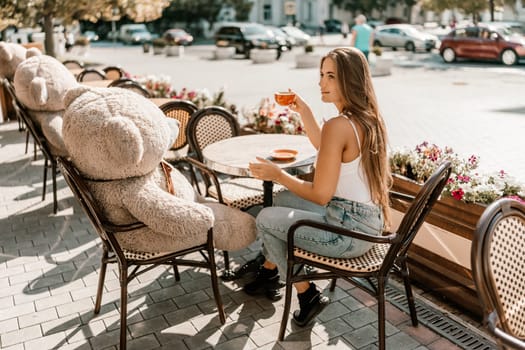 Portrait of happy woman sitting in a cafe outdoor drinking coffee. Woman while relaxing in cafe at table on street, dressed in a white T-shirt and jeans.