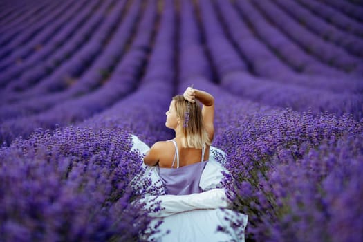 A middle-aged woman sits in a lavender field and enjoys aromatherapy. Aromatherapy concept, lavender oil, photo session in lavender.