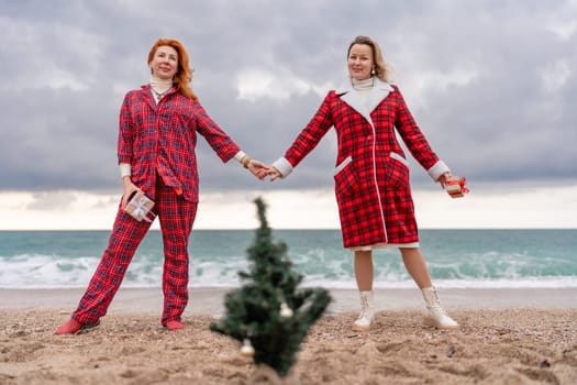 Sea two Lady in plaid shirt with a christmas tree in her hands enjoys beach. Coastal area. Christmas, New Year holidays concep.
