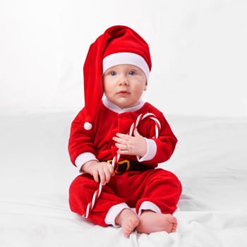 Baby, portrait and cute with santa outfit for first Christmas holiday, candy cane and white background. Boy toddler, xmas and costume for festive season or celebration, innocent and adorable with hat.