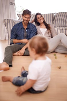 Family, couple and smile in lounge with toddler for growth, development and bonding on floor. Parents, caregivers and happy with little boy or child in home for activities, games and playing.