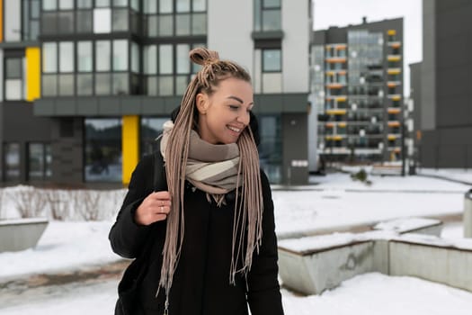 Smiling cute woman with blond dreadlocks wearing a black long winter jacket.