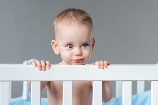 A child stands in a crib and looks with sarcasm like an adult.