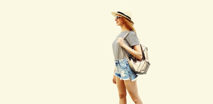 Portrait of smiling young woman wearing summer straw hat, backpack and shorts on white background