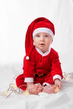 Baby, portrait and cute with santa costume for first Christmas holiday, star lights and white background. Boy toddler, xmas and outfit for festive season or celebration, innocent and adorable in hat