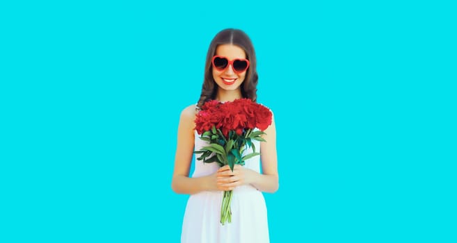 Portrait of beautiful smiling woman with bouquet of red rose flowers in heart shaped sunglasses on blue background