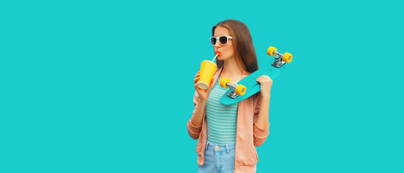 Portrait of stylish young woman with skateboard drinking juice on blue background