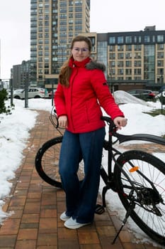 Cute young woman in a winter jacket rides a bicycle on the bike path.