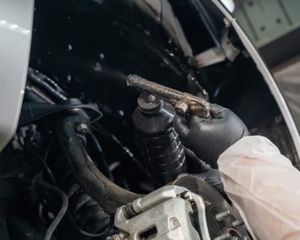 An auto mechanic applies anti-corrosion mastic to the underbody of a car