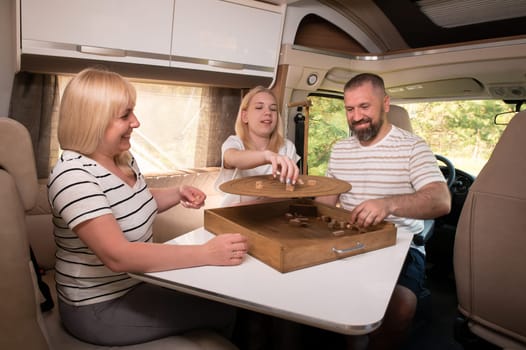 A family of three is playing a board game while sitting in a motorhome.