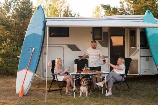 A happy family is resting nearby near their motorhome in the forest.