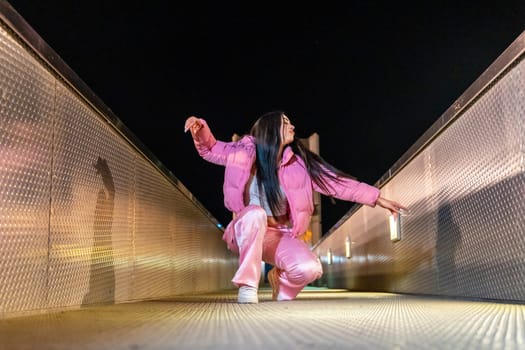 Low angle view photo of a happy dancer in squatting position on a bridge at night