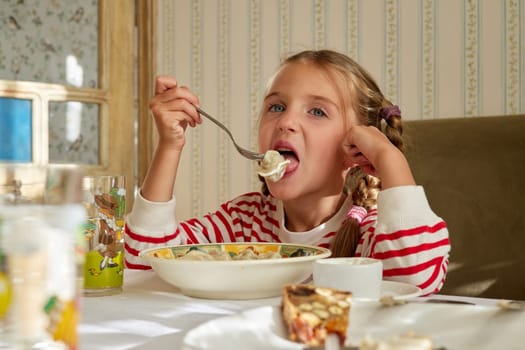 Hungry girl eats homemade dumplings dipped in sour cream. Enjoyment of dish and satisfying hunger. Spending holidays in village in summer