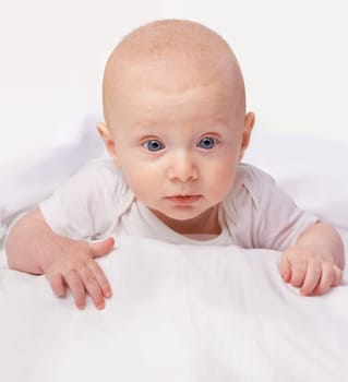 Baby, blue eyes and shock with laying on bed for curiosity, surprise and reaction in bedroom at house. Adorable, child and cute infant with vest in home to observe, relax wonder for knowledge.