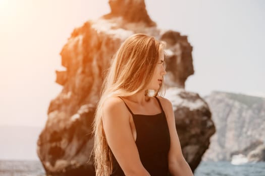 Woman travel sea. Young Happy woman in a long red dress posing on a beach near the sea on background of volcanic rocks, like in Iceland, sharing travel adventure journey