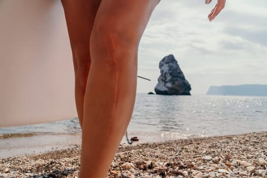 Close up shot of beautiful young caucasian woman with black hair and freckles looking at camera and smiling. Cute woman portrait in a pink bikini posing on a volcanic rock high above the sea