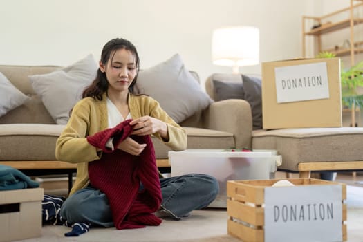 Woman asian holding donation box full with clothes and select clothes. Concept of donation and clothes recycling. Helping poor people.