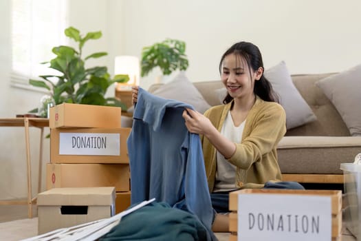 Woman asian holding donation box full with clothes and select clothes. Concept of donation and clothes recycling. Helping poor people.