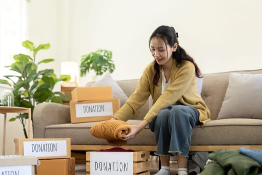 Woman asian holding donation box full with clothes and select clothes. Concept of donation and clothes recycling. Helping poor people.